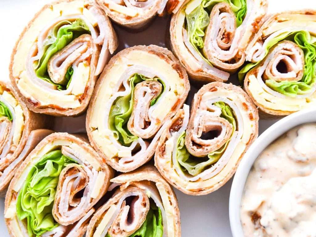 close up of group of turkey pinwheels with a bowl of cream cheese dip